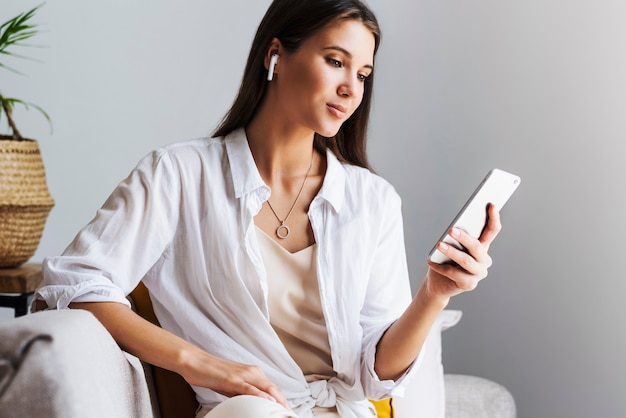 Female relaxing at home, using smartphone to text messages, share photos, communicate with friends, check email, watch videos, play games online. Entertainment opportunities on web connected gadgets.