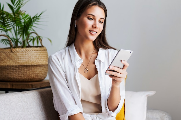 Female relaxing at home, using smartphone to text messages, share photos, communicate with friends, check email, watch videos, play games online. Entertainment opportunities on web connected gadgets.