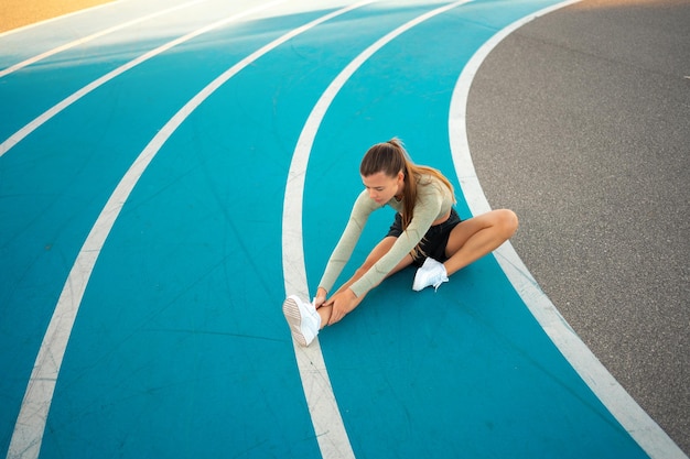 Female runner doing stretching exercises sitting on running track