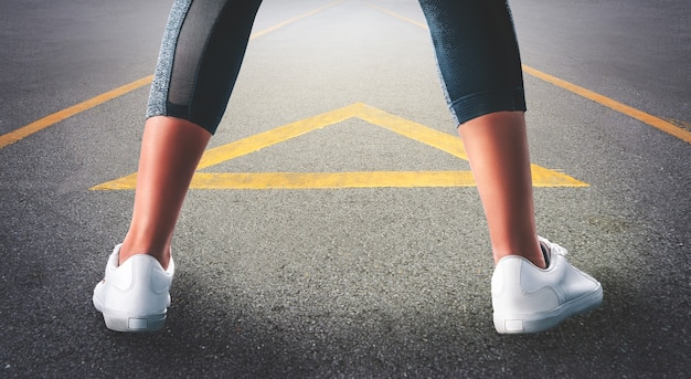 Female runner Legs spreading getting ready to work out on the road with arrow direction.