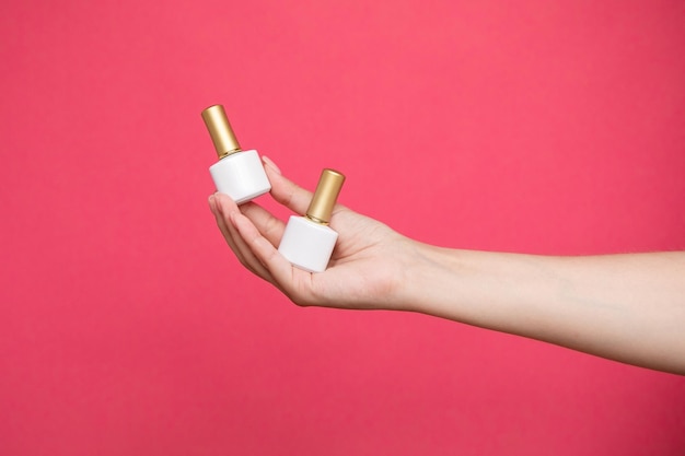 Female's hand holding bottles nail polish on pink background.