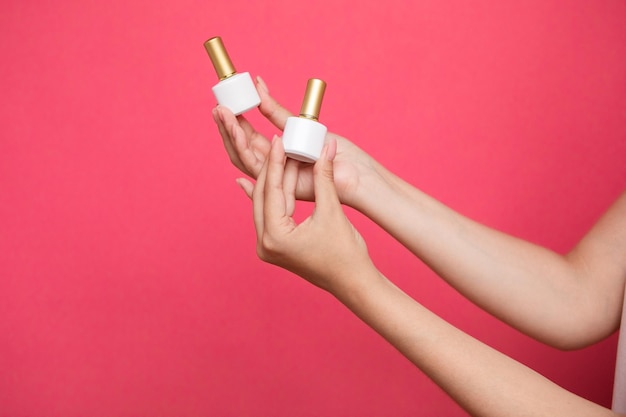 Female's hands holding bottles nail polish on pink background.