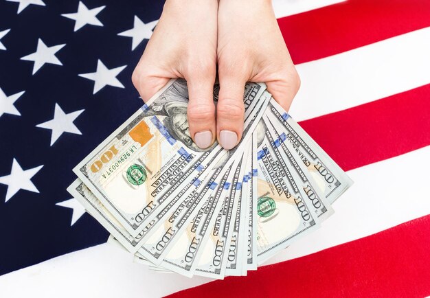 Female's hands holds dollar bills over background of american flag