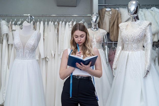 Female saleswoman holding a notebook and posing in a salon selling wedding dresses