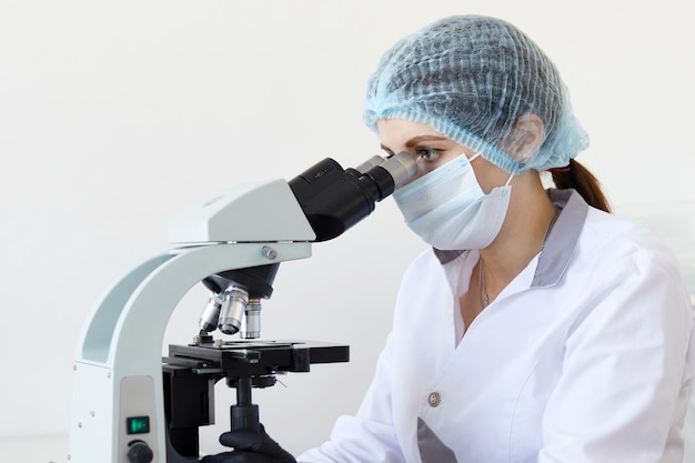 Female scientist looking through microscope in modern chemical laboratory doing some research