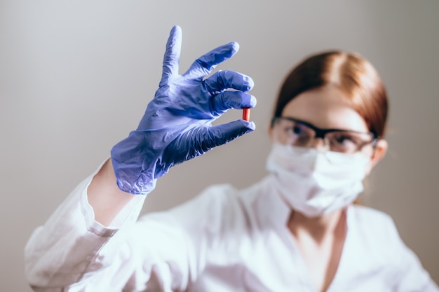 Female scientist with protective mask shows a medicine pill. Novel innovated treatment concept. The concept for health