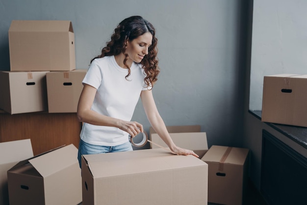 Female sealing cardboard box parcel with adhesive tape on moving day Removal service relocation