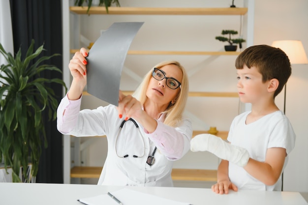 Female senior pediatrician showing xray of wrist and hand to little boy patient Child at doctors office