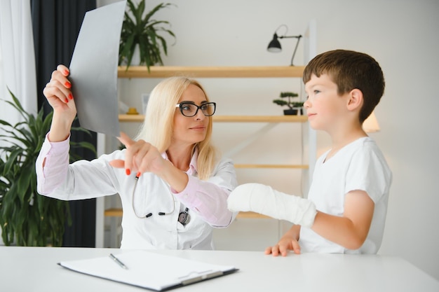 Female senior pediatrician showing xray of wrist and hand to little boy patient Child at doctors office