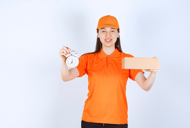 Female service agent in orange color dresscode holding a cardboard box and an alarm clock