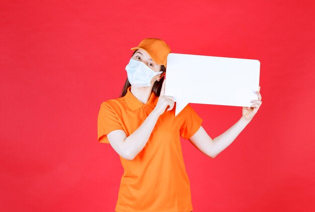 Photo female service agent in orange color dresscode and mask holding a white rectangle info board.