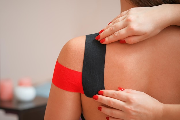 Female shoulder with applied red kinesiology tape