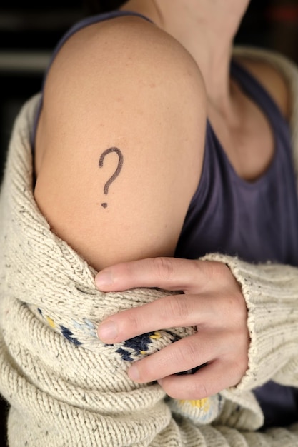 Female shoulder with a drawn question mark. Concept of uncertainty to vaccinate against covid