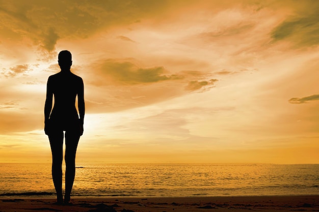 A female silhouette against an orange sky a lonely woman looks at the evening sunset on the beach by