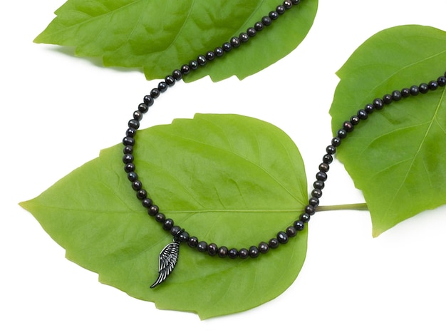 Female silver wing shaped pendant with black beads chain necklace on green leaves Closeup shot