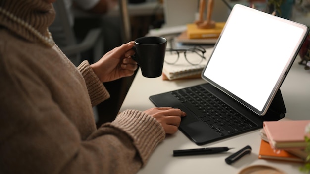 Female sipping coffee while working on her portable tablet computer in her home office Remote work