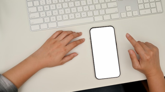 A female sits at her working desk smartphone mockup and keyboard on white table overhead