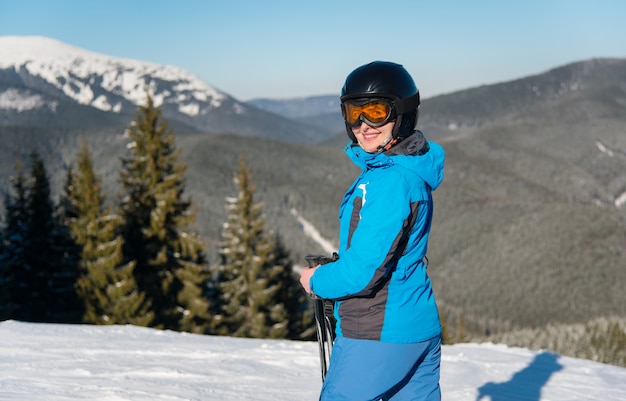 Female skier smiling to the camera joyfully while skiing in the mountain on a sunny winter day