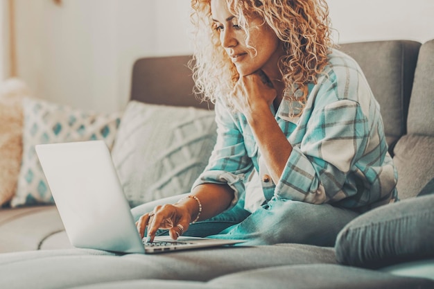 Female smile and use laptop sitting on the sofa People enjoying online activity working on computer Woman using notebook in indoor connection leisure activity Smart working free office job