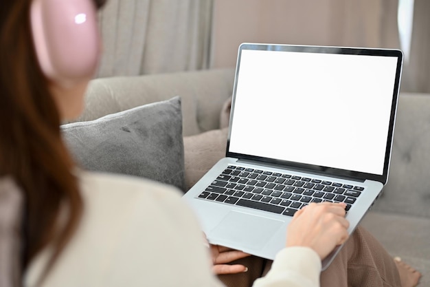 Female on sofa in living room wearing headphones and using laptop Laptop white screen mockup