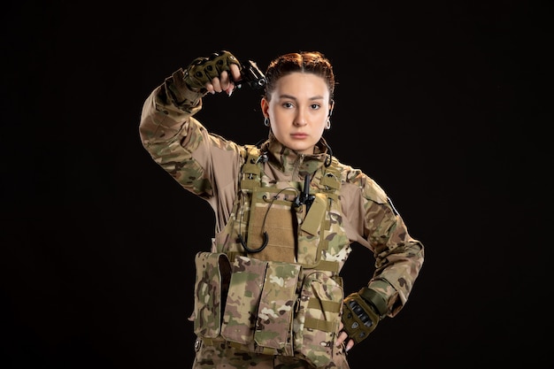 Female soldier in camouflage aiming gun on the black wall