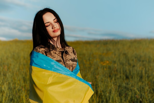 Female soldier dressed in military uniform wrapped in ukrainian flag