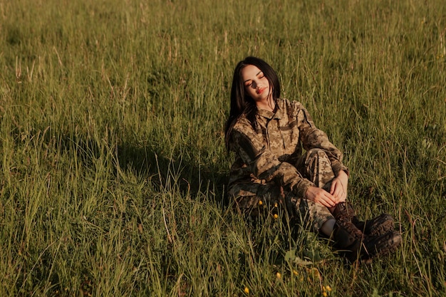 Female soldier sitting on grass in the field dressed in military uniform