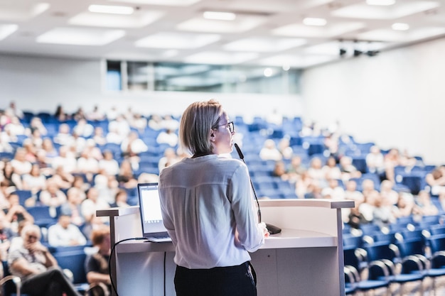 Female speaker giving a talk on corporate business conference Unrecognizable people in audience at