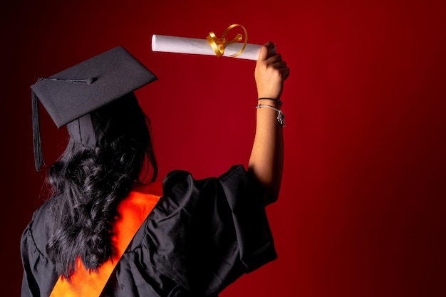 Female student in a graduation photo End of education degree with graduate diploma University tunic with cap on his back with the diploma copy space