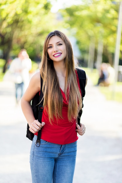 Female student holding a book outdoor in the park and smiling