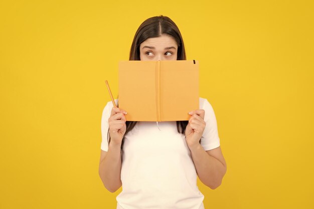 Female student holds books isolated on yellow background in studio English language school education