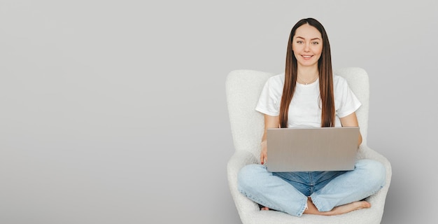 Female student sits in a chair with a laptop smiling and looking at the camera