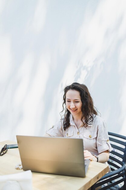 A female student sits on the summer terrace of a cafe and works at a laptop Female freelancer works remotely online while sitting in a summer cafe Remote work