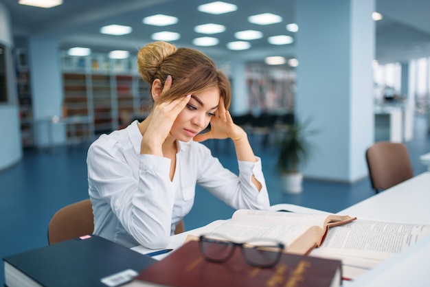 Female student studying book at the table in library.