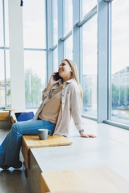 A female student works in a bright cafe with large windows online Remote work with a laptop in a cozy work cafe