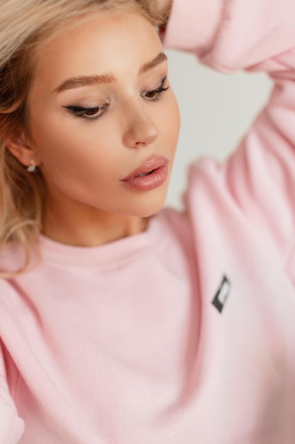 Female studio portrait of a beautiful young stylish woman with a cute face in a fashionable pink sweatshirt