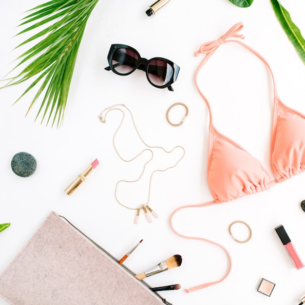 Female summer bikini swimsuit and accessories collage on white with palm branches, necklace and sunglasses.