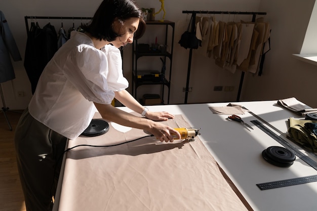 Female tailor cut material for garment with professional electric cutter machine in atelier studio