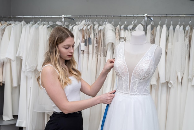 Female tailor use measuretape for measure new wedding dress on mannequin in store