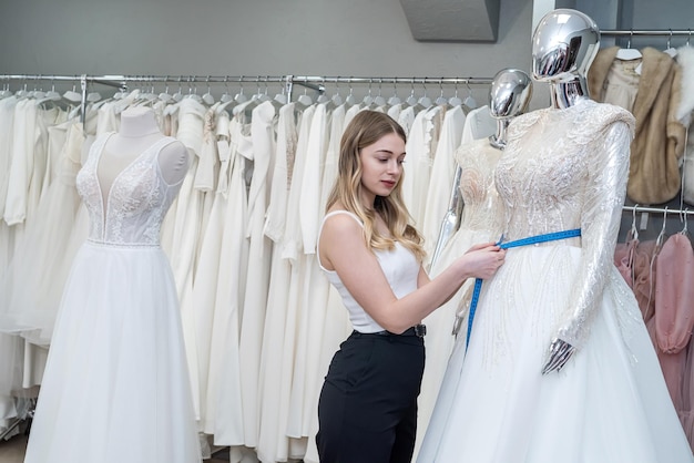 Female tailor use measuretape for measure new wedding dress on mannequin in store