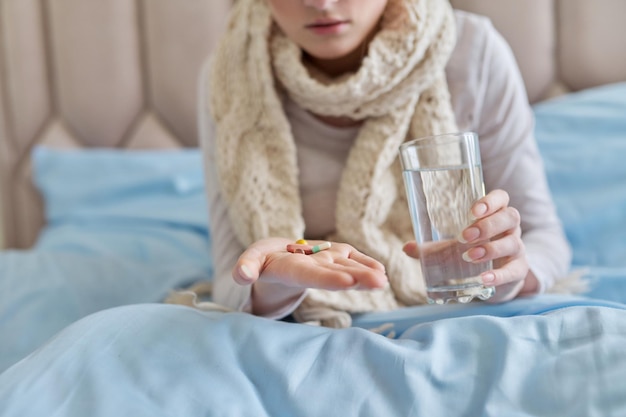 Female taking pills capsules with glass of water at home in bed