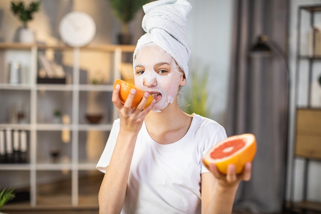 Female teenager with mask on face biting slice of grapefruit