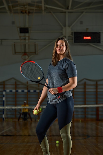 Female tennis player with racket and ball on gym background