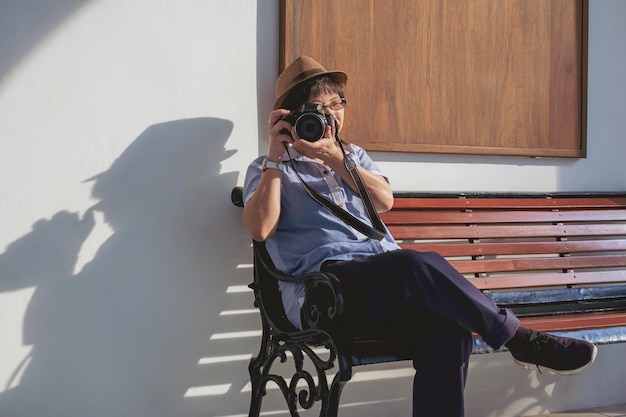 Female tourist photographing with digital camera while sitting on bench outside of vintage building