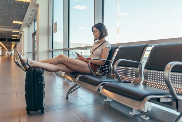 Female tourist sitting on bench with baggage in waiting room at airport