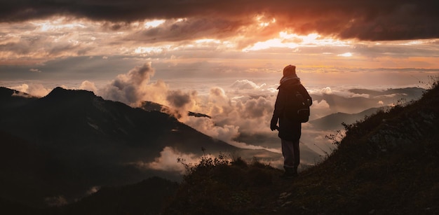 Female tourist with a backpack in autumn on the mountain with outstretched arms welcomes admires the sunset