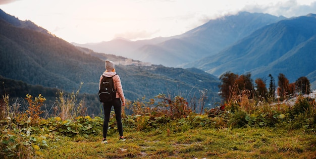 Female tourist with a backpack enjoys the sunset at the top mountain