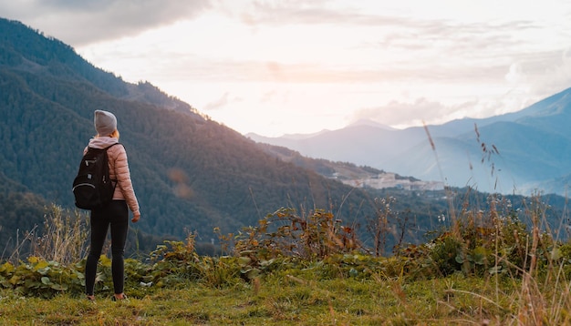 Female tourist with a backpack enjoys the sunset at the top mountain