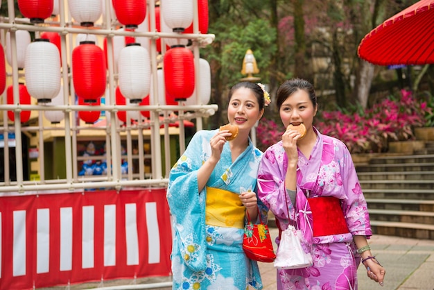 female tourists going to japan participate famous festivals celebrating wearing traditional kimono and eating delicious dorayaki food together walking in the streets of cultural lanterns.