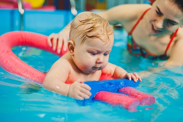 A female trainer teaches a baby to swim in the pool and supports his hands Baby swimming in the pool Teaching a newborn boy to swim in the pool